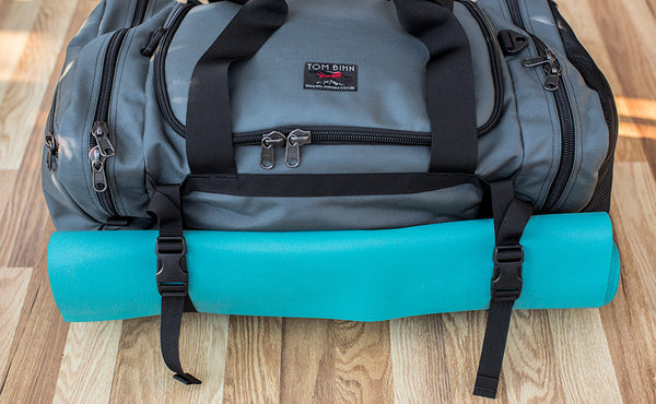 The Road Buddy Lash Straps holding a rolled yoga mat on a Road Buddy Duffel 60.